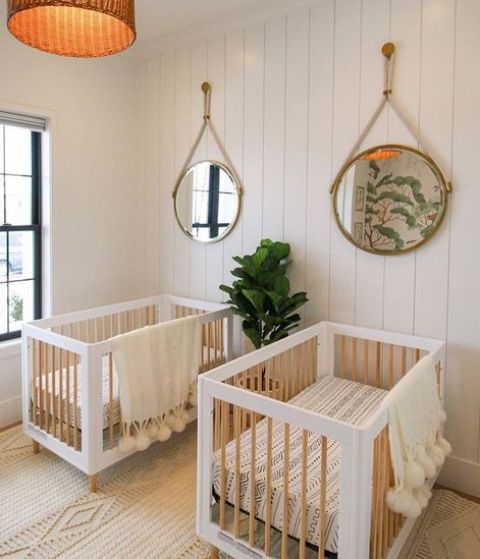 a neutral modern twin nursery with white beadboard walls, white and stained cribs, round mirrors, a pendant lamp and neutral textiles