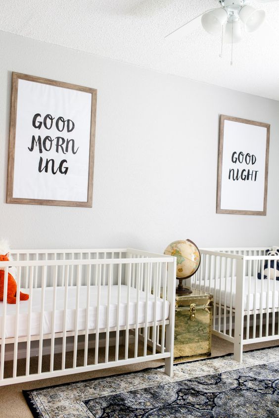 a neutral twin nursery with white cribs, a printed rug, a gilded chest with a globe and a mini gallery wall