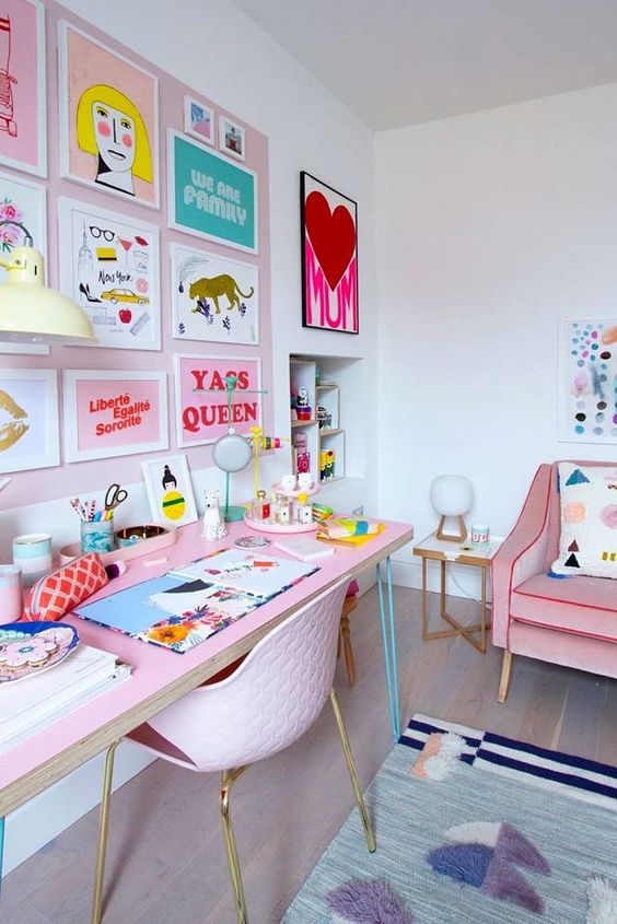 a pastel maximalist home office with a blush accent wall and a colorful gallery wall, a pink desk and a pink chair, a pink sofa and colorful textiles