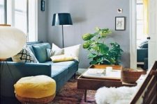 a pretty living room with grey walls, a turquoise sofa, some rattan and wooden furniture, a printed rug and a potted plant