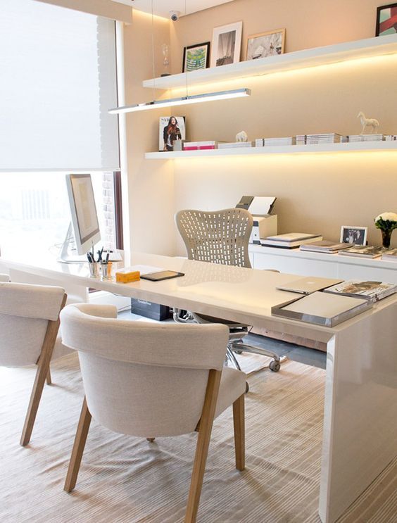 A refined contemporary home office with a large white desk, comfy neutral chairs, open shelves with built in lights and a credenza