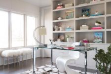 a refined home office with built-in storage units and shelves, a clear glass desk, a white sculptural chair and faux fur stools