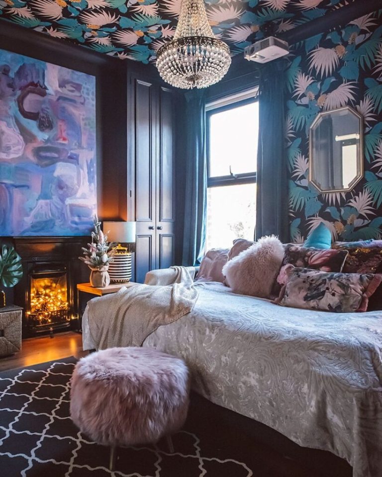 a refined maximalist bedroom with dark walls, a printed ceiling, a fireplace with lights, a statement artwork and a daybed with pillows