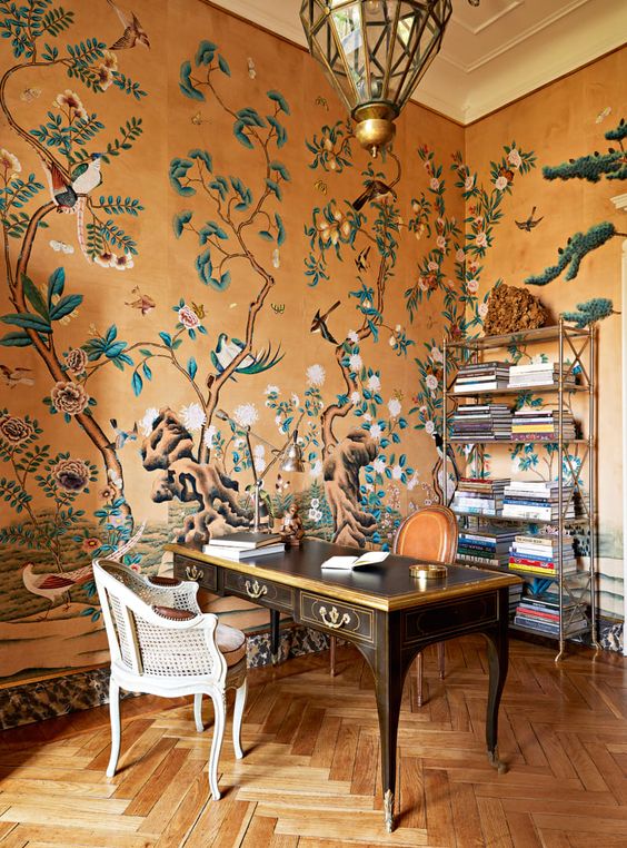 a refined maximalist home office with beautiful wallpaper walls, a refined vintage desk, a rattan chair, a chic faceted pendant lamp and an open storage unit