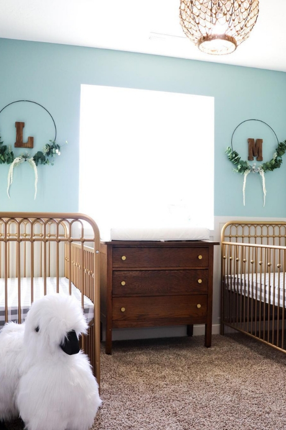 a retro-inspired twin nursery with blue walls, metal cribs, a stained dresser, a rug and some pretty wreaths on the wall