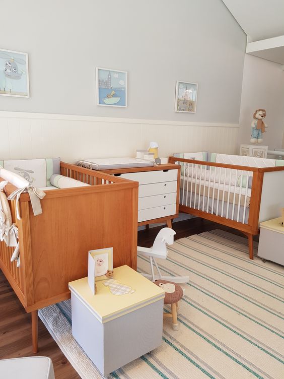 A retro inspired twin nursery with stained cribs, a stylish dresser, some pretty kids' furniture and a lovely gallery wall