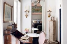 a sophisticated home office with a vintage bureau desk, a sheer blush chair, vintage lamps and candleholders on the walls