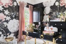 a sophisticated home office with moody floral wallpaper, a black and gold desk, chic tufted chairs, black storage units and a sunburst chandelier