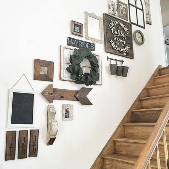 a stylish gallery wall with wooden arrows and signs and artworks in stained frames, mirrors and vintage window frames