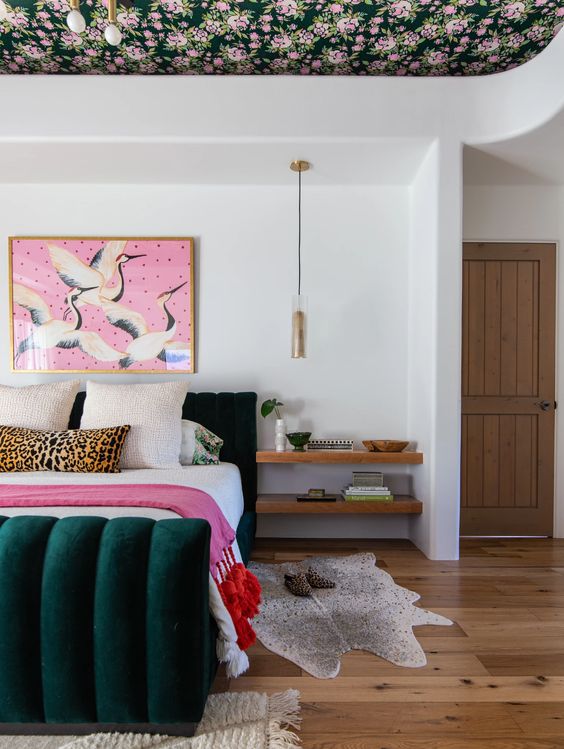 A stylish maximalist bedroom with a floral ceiling, a dark green velvet bed, a bold artwork and pretty rugs plus pendant lamps