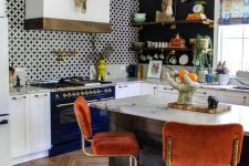 a stylish maximalist kitchen with black walls and an accent tile one, white cabinetry and a navy cooker, rust chairs and a marble countertop