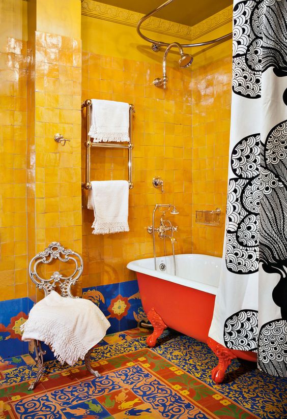 a super bold maximalist bathroom with bold yellow and blue tiles, colorful mosaic tiles on the floor, a red bathtub, a vintage chair