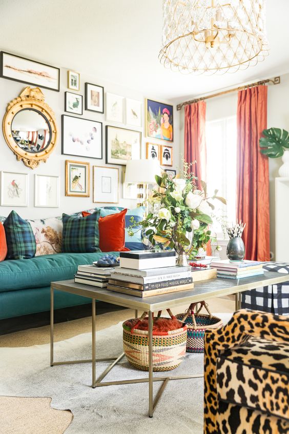 an airy maximalist living room with neutral walls, a green sofa, a large coffee table, a leopard print chair, coral curtains and a lovely chandelier