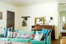 an eclectic living room with a turquoise sofa, a rough wooden table, a chair, a wooden dresser and some mirrors on it
