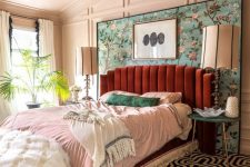 an elegant maximalist bedroom with paneled walls, a burgundy velvet bed, a printed carpet, pastel bedding and a lovely crystal chandelier