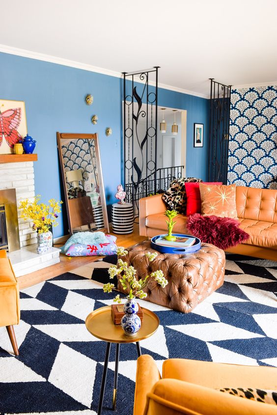 bright maximalist living room with blue walls, a chevron rug, an amber sofa and an ottoman, yellow chairs, a gold table and a fireplace
