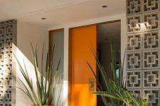 03 a very chic mid-century modern front porch with a bold orange door and planters with oversized plants plus screens to protect from the sun