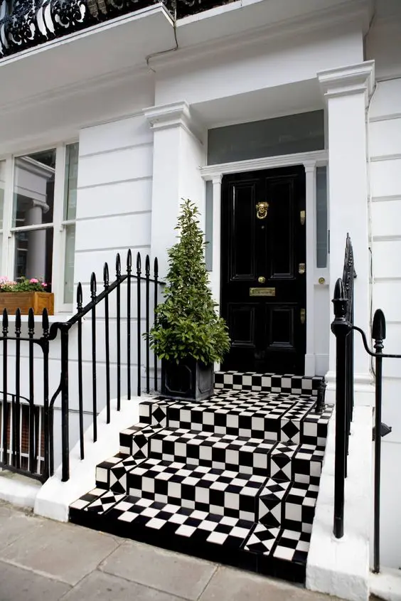 a chic and cool modern front porch with a black door, gold detailing, black and white tiles and a mini Christmas tree in a black planter