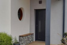 10 a modern and laconic front door porch with a bench with rocks inside, greenery in pots and a stylish door