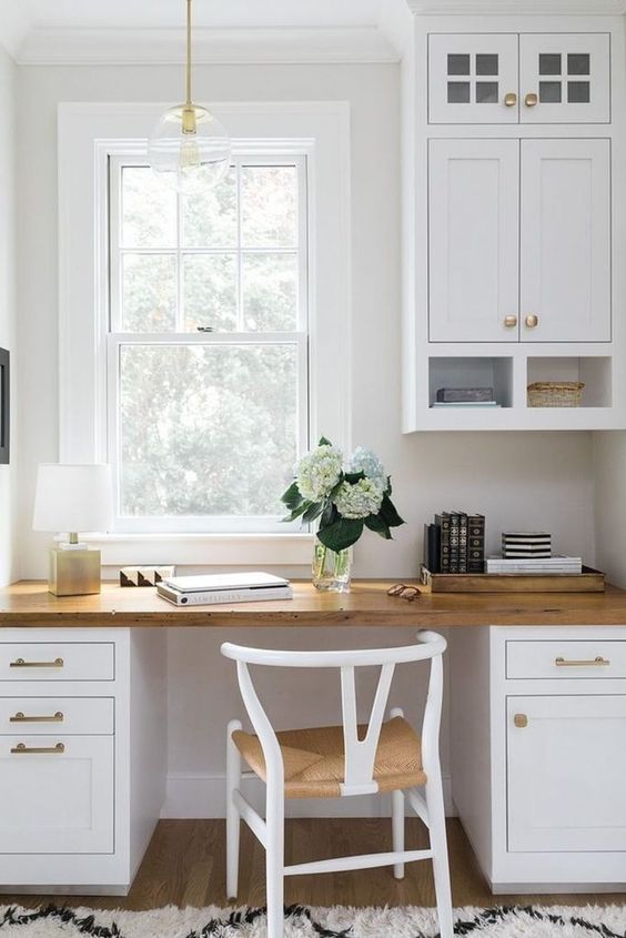 a welcoming white farmhouse home office done with kitchen cabinets and a matching desk, a woven chair and a pendant lamp