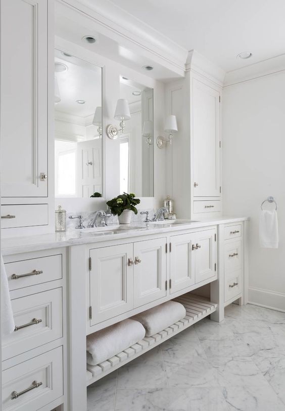 a gorgeous master bathroom with creamy shaker style cabinets from the kitchen, a double mirror and sink, sconces and a chic floor