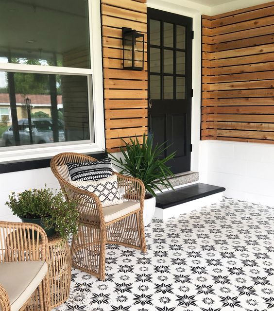 A modern porch clad with pretty star patterned tiles, with rattan chairs, potted greenery and a black door and steps is a chic idea