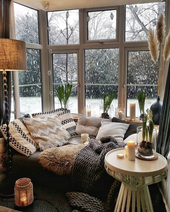a Scandinavian nook with a corner window, a daybed with lots of pillows and blankets, candles and candle lanterns