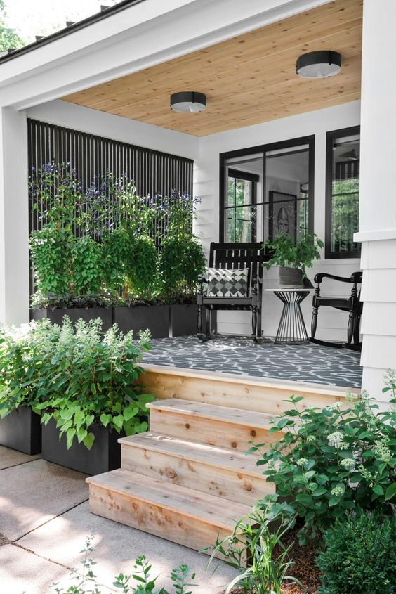 a modern porch with a cool printed rug, potted greenery, black rockers and a coffee table plus ceiling lamps is amazing