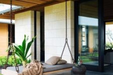 23 a modern porch with a swinging daybed on chains and a carved wooden side table feels and looks very zen-like