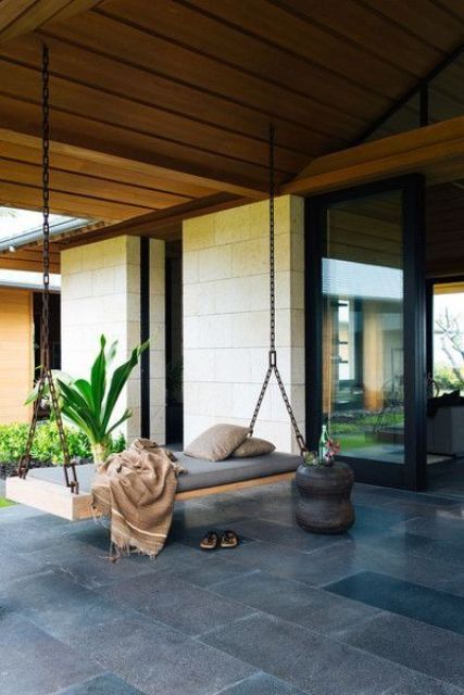 A modern porch with a swinging daybed on chains and a carved wooden side table feels and looks very zen like