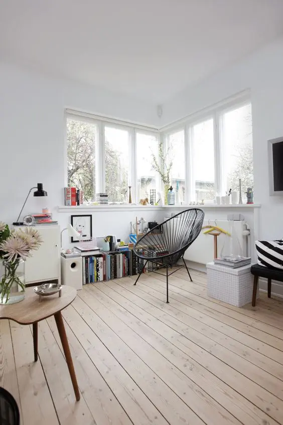 a lovely Nordic nook with a corner window, a windowsill used for storage, a black chair and a bookshelf is a very cozy corner