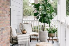 a modern porch with rattan chairs, a jute pouf, potted plants, a magazine stand and some neutral textiles is very chic