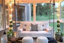 27 a welcoming modern porch with a suspended sofa, matching poufs, potted plants, candle lanterns and a bold geometric rug plus lights over the space