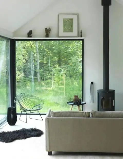 a contemporary living room with a corner window for gorgeous forest views, a hearth and cool furniture, some artworks over the window