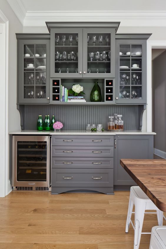 a chic grey home bar with kitchen cabinets - glass and usual ones, a beadboard backsplash and a wine cooler