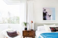 32 a gorgeous modern boho bedroom with a corner window, an upholstered bed, bright bedding and boho touches plus a chair by the window