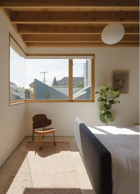 a simple and minimal bedroom with a corner window that brings natural light inside, with a chair and an upholstered bed