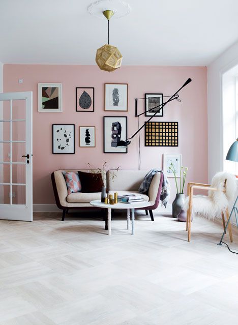 a Scandinavian living room with a light pink accent wall and a gallery wall, a chic sofa, a wooden chair and a coffee table plus a faceted lamp