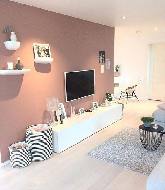 a Scandinavian living room with a mauve accent wall, a sleek TV unit, some fabric baskets and shelves for decor on the accent wall