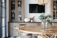 a beautiful modern country dining room with a checked floor, a round table, vintage chairs, a wooden bead chandelier and storage cabinets