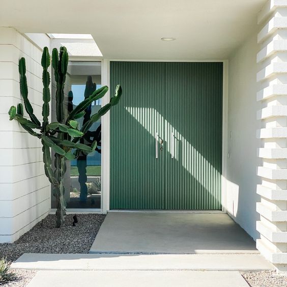 a beautiful modern entrance with green fluted doors and a cactus planted by the window is a cool and laconic space