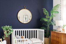 a beautiful modern nursery with a navy accent wall, chic mid-century modern furniture, a printed rug, a basket for storage, potted plants and a chic chandelier