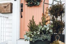 a beautiful modern rustic porch with a coral door, a greenery wreath, potted greenery, a firewood stand, a gold candle lantern
