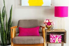 a bold interior with a grey chair, a crate side table, a potted plant, a bright artwork and touches of hot pink in accessories