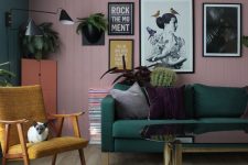 a bold living room with a pink planked accent wall, a dark green sofa and a wall, a mustard chair, some greenery and touches of black for drama