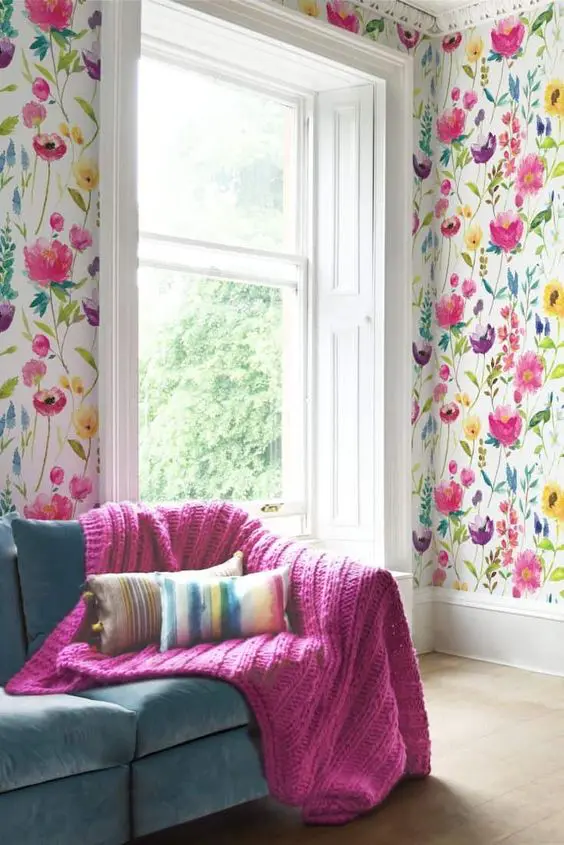 a bold living room with floral wallpaper, a teal sofa and a hot pink blanket that echoes with the floral patterns on the wall