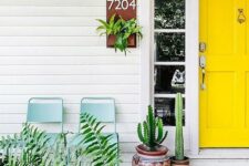 a bright modern porch with a sunny yellow door, cacti in pots and greenery and blue chairs to relax here