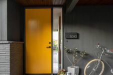 a bright modern porch with an orange door, potted plants, a watering can and a house number is a chic and bold space