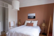 a catchy bedroom with a mauve accent wall, a comfy bed, woven floor lamps and a pendant lamp with a white lampshade