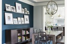 a chic farmhouse dining room with a navy accent wall, dark stained furniture, a gallery wall on ledges and a sphere pendant lamp